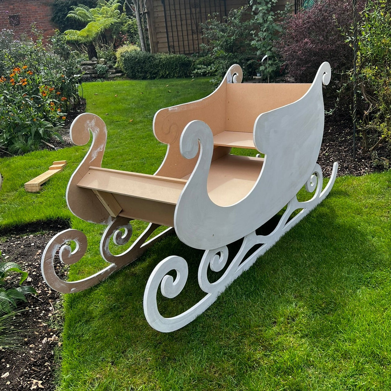 Wooden sleigh on a grassy lawn with a garden background